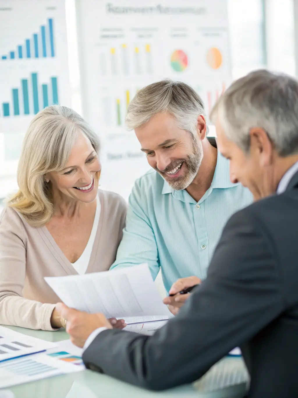 A professional financial advisor in a modern office setting, explaining retirement planning options to a middle-aged Indian couple, with charts and graphs visible on a nearby screen.